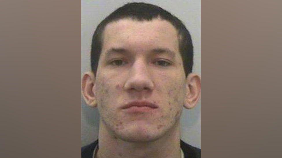 Custody shot of Anthony Ellis from 2013. He has short cropped dark hair and acne.