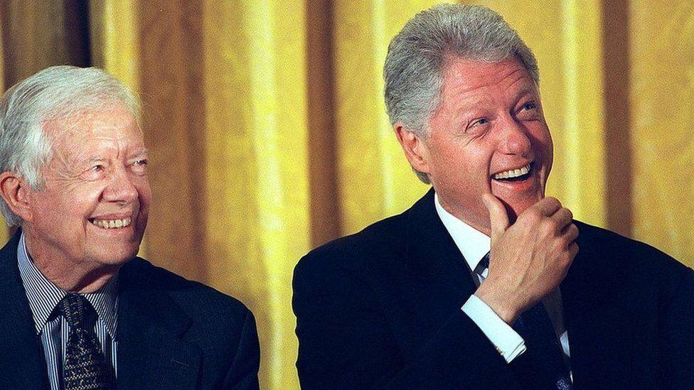 US President Bill Clinton smiles as he listens to speakers with former US President Jimmy Carter in front of a yellow curtain during a rally in 2000 in support of permanent normal trade relations (PNTR) with China. 