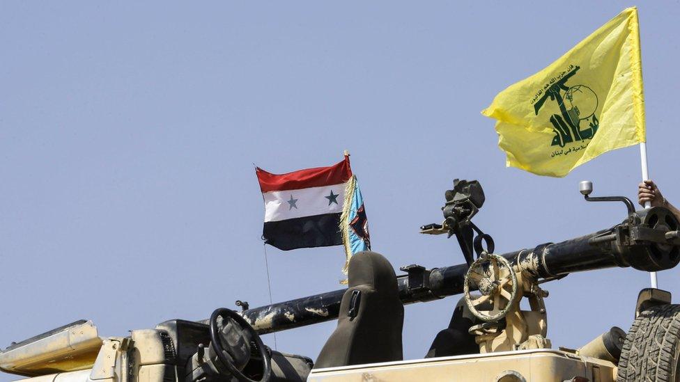 A picture taken on August 2, 2017 during a tour guided by the Lebanese Shiite Hezbollah movement shows the flags of the movement (R) and the Syrian national flag (L) flying by a four-wheel drive vehicle carrying a recoilless rifle, at a position in a mountainous area around the Syrian town of Flita near the border with Lebanon.