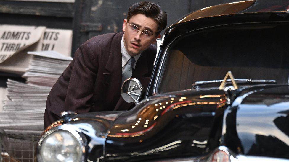 Timothée Chalamet is seen on the set of "Marty Supreme" in Midtown Manhattan on October 02, 2024 in New York City, wearing a suit and glasses and leaning down to a taxi window