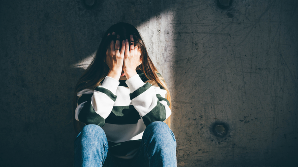 Young woman holding head in hands against concrete wall (stock image)