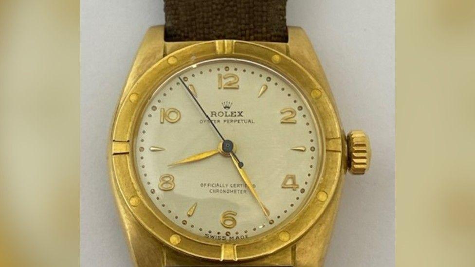 A close up image of an 18ct gold Rolex watch face with a brown canvas strap.