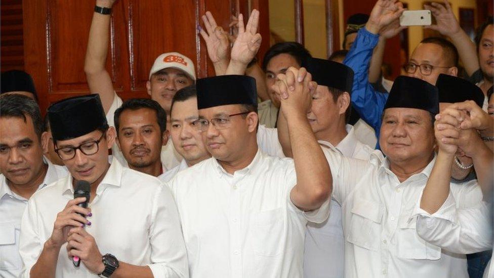 Jakarta governor-elect Anis Baswedan (C), his deputy governor-elect Sandiaga Una (L) and Prabowo Subianto (R) of the Gerindra party hold hands together during a press conference in Jakarta on April 19, 2017