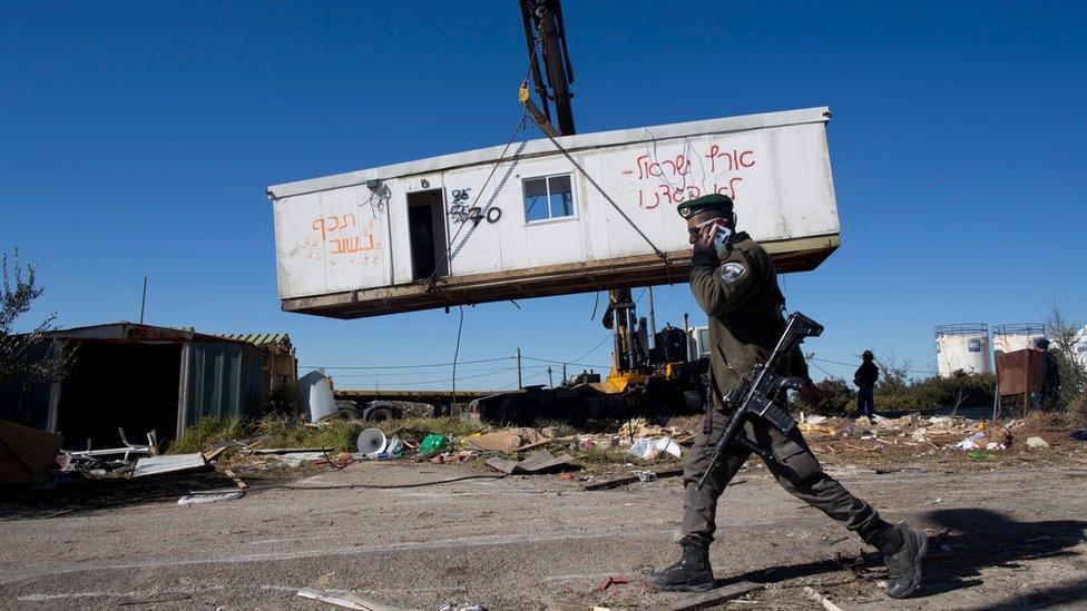 An Israeli border policeman walks near workers lifting a housing unit with a crane during the demolition of the unauthorised Jewish settlement outpost of Amona (7 February 2017)