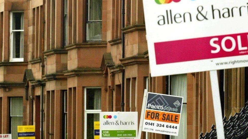 A close up of a row of red/brown sandstone houses with placard for sale signs for different estate agents in the street