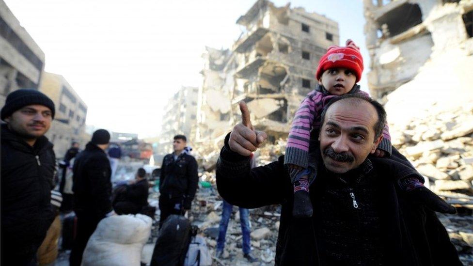 People, who evacuated the eastern districts of Aleppo, stand with their belongings in a government-held area of Aleppo, Syria on 9 December 2016.