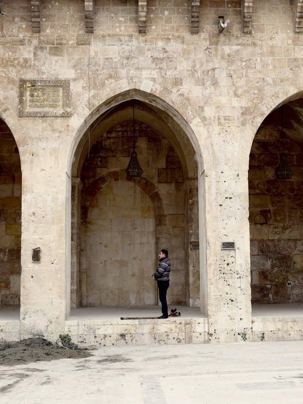 A man can be seen praying inside one of the arches of the mosque