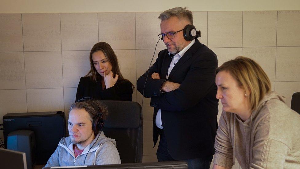 Journalists from TVP-Info stand around a computer in a bathroom