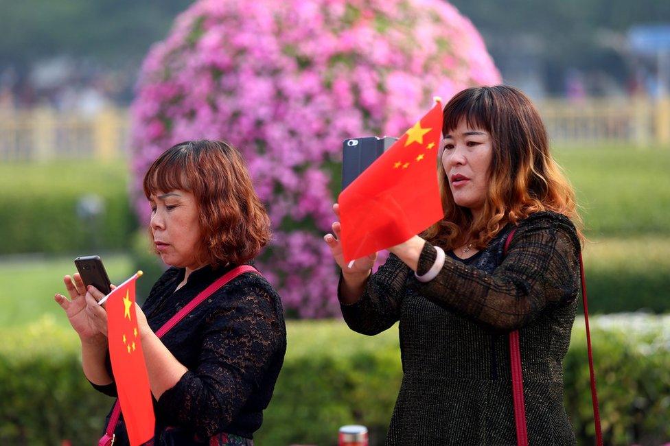 Tourists holding Chinese national flags use mobile phones to take photos at Tiananmen Square during National Day celebrations in Beijing, China, 1 October 2016.