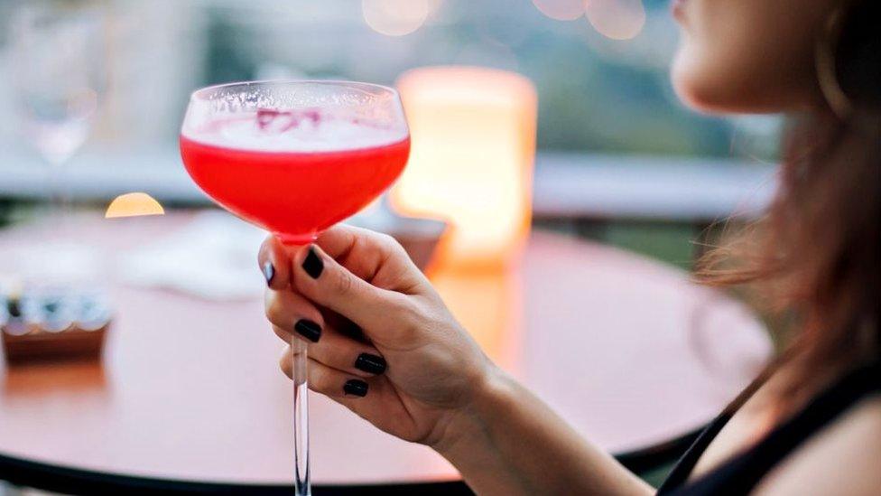 A woman sits alone with a drink