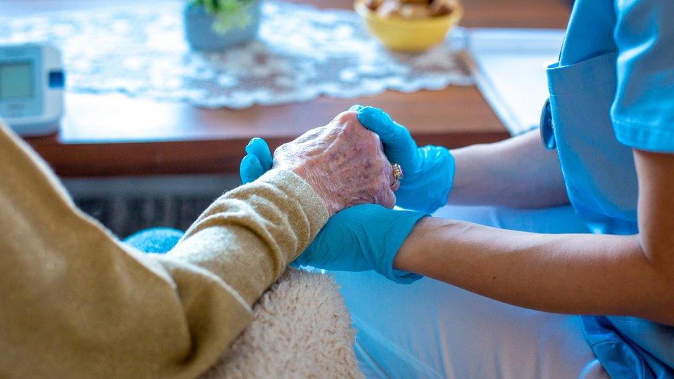 A carer holding the hand of an elderly person