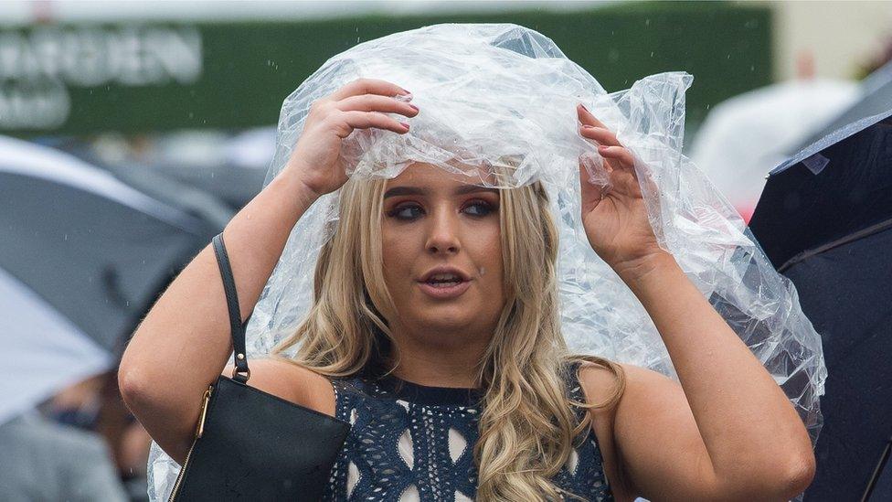 A woman shields her hair from the rain under a large plastic bag