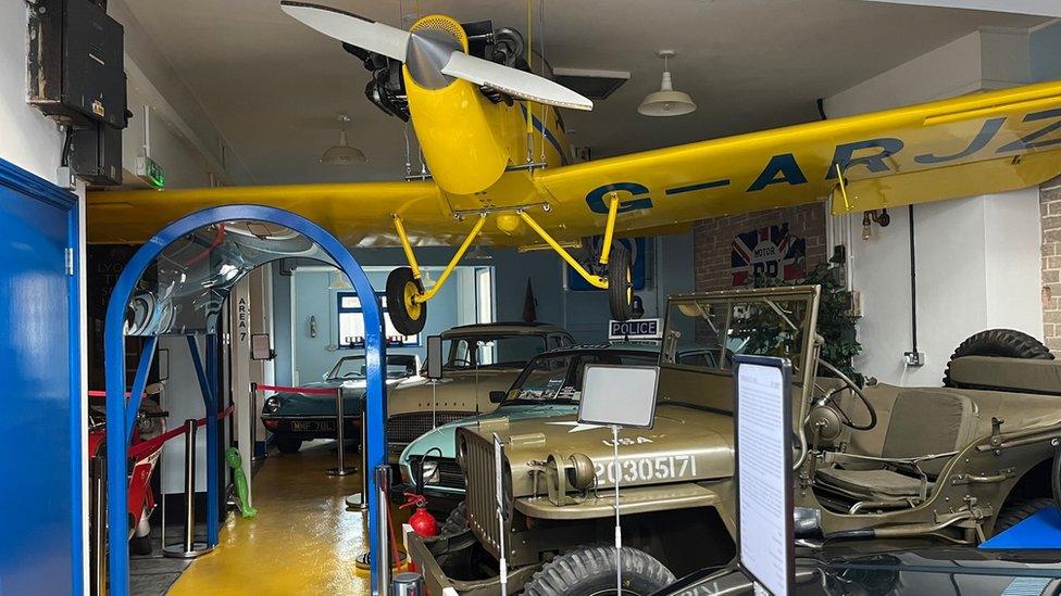 The inside of the car museum with a plane hanging from the ceiling