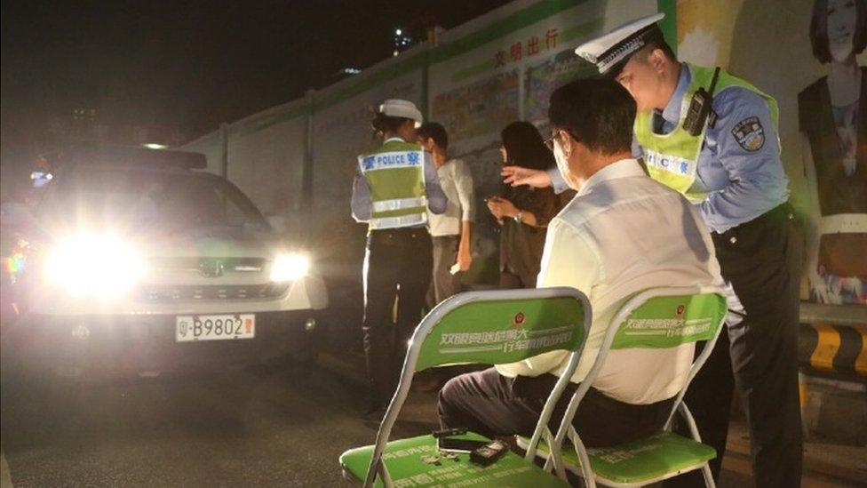 Shenzhen Traffic Police photo showing a man on a chair in the beam of car headlights with a police officer next to him