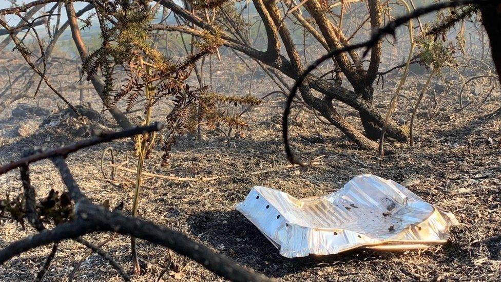 An upturned foil barbecue laying in a charred landscape