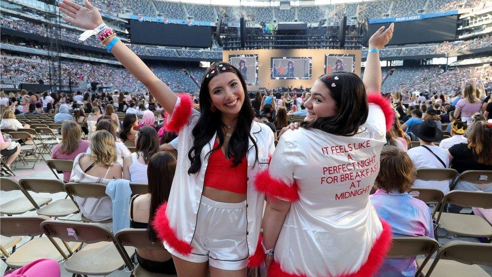 Two fans at a concert - one wearing clothes which read Taylor Swift lyrics