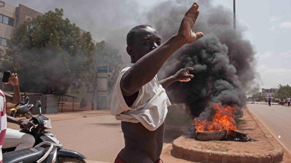 A Burkina Faso protestor gestures in front of burning tires as he and others take to the streets in the city of Ouagadougou, Burkina Faso, Thursday, 17 September 2015