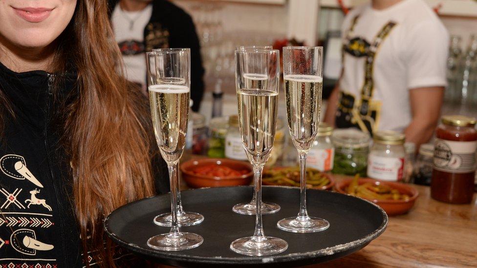 A woman holding a tray of prosecco glasses