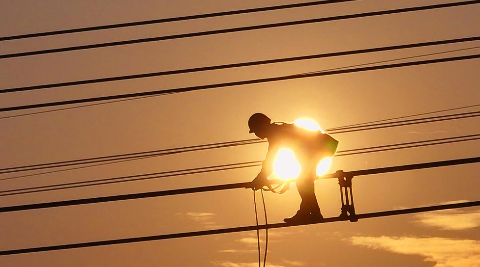 An electrician carries out maintenance work on electric wires of a 500KV transmission line project at sunset in Lianyungang, Jiangsu Province of China on 28 September 2022.