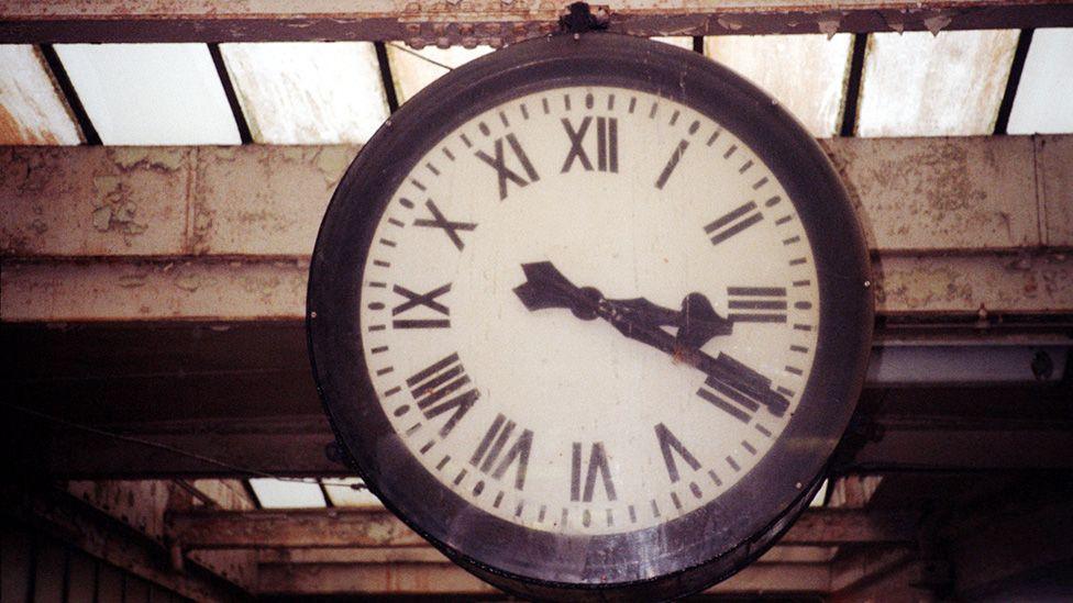 The station clock -  a large white clock with thick black hands and rim, and Roman numerals.