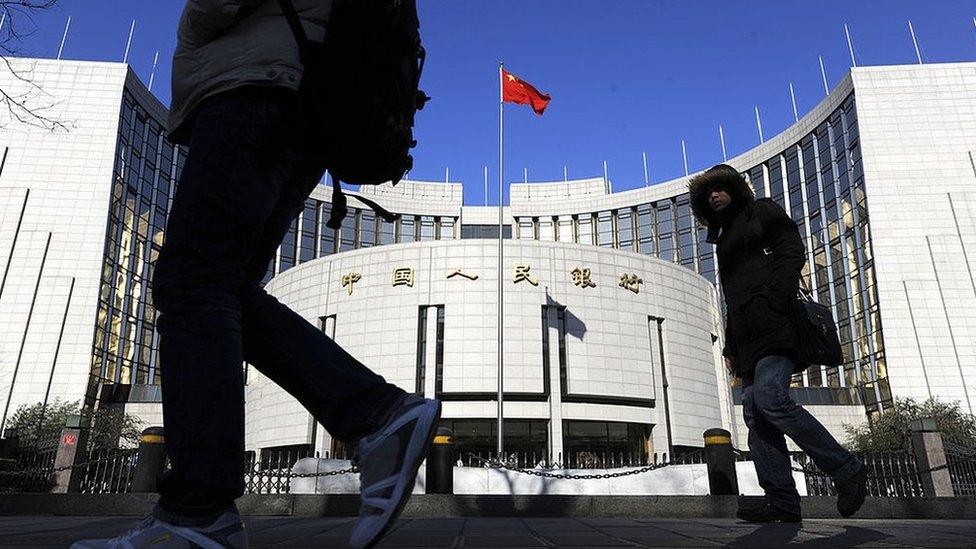 Two pedestrians walk in front of the headquarters of the People's Bank of China in Beijing