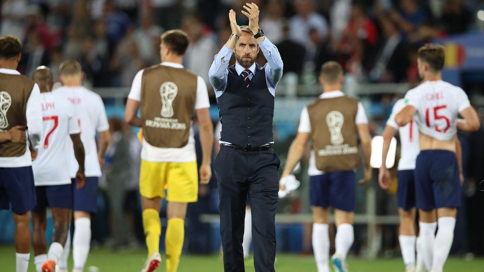 Gareth Southgate is clapping his hands in the air whilst some of the England players walk off the pitch