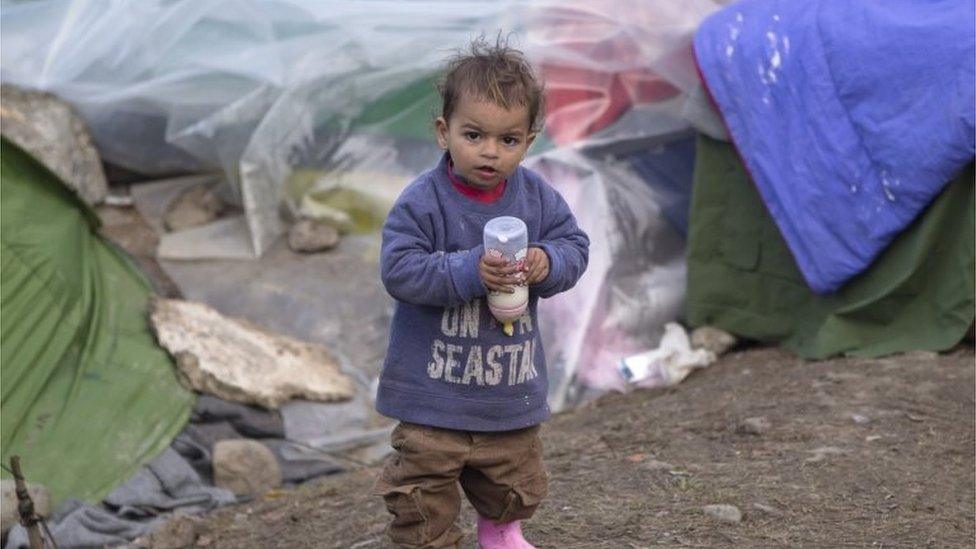 A toddler of a migrant family holds a baby bottle with milk at a makeshift camp in Idomeni, Greece. Photo: 18 March 2016