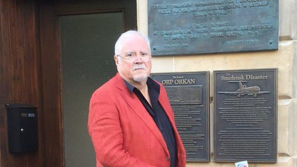 Anthony Kozlowski stands on the steps of the Sikorski Polish club in Glasgow, in front of memorial plaques.