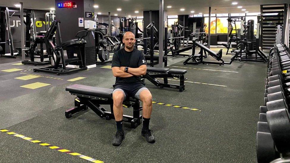 Gym manager Rob Ward sitting in his gym with yellow tape marking floor areas.