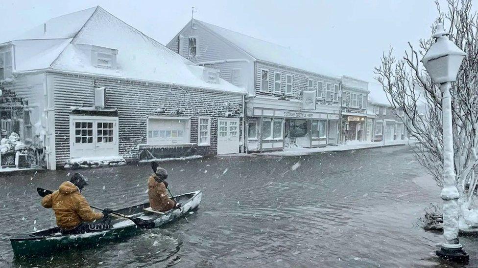 High School students row a canoe along a road during heavy flooding, in Nantucket, Massachusetts