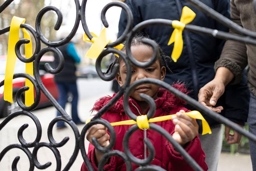 A girl ties a yellow ribbon to a railing