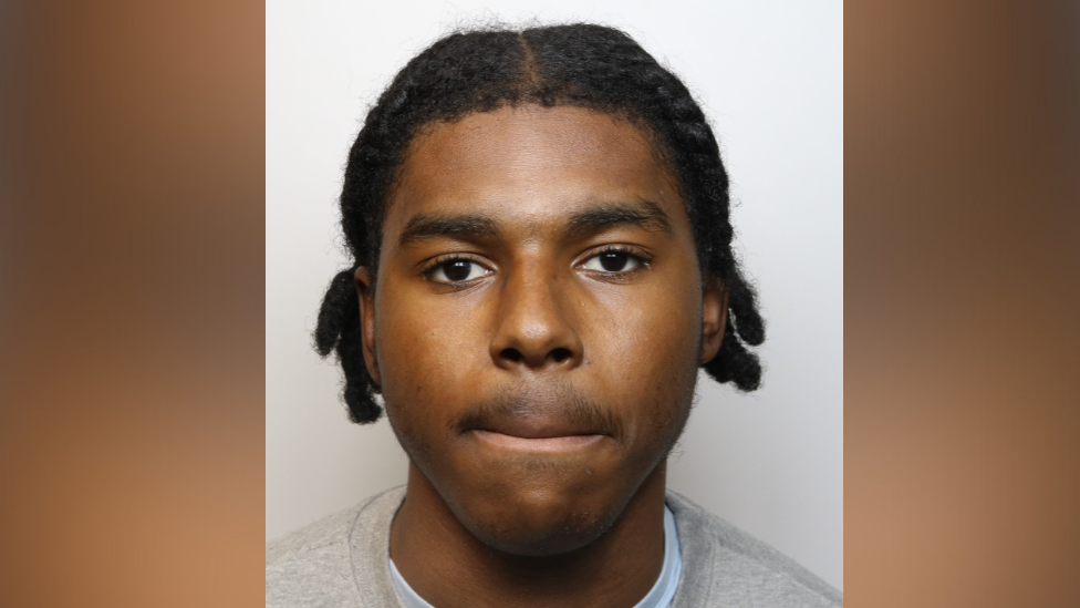 Custody image of Jaredel Comrie. He is wearing a grey jumper.