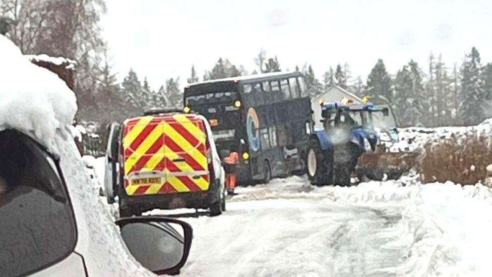 An image of a double decker bus which appears to be stuck on an Aberdeenshire road, a tractor and other vehicles can also be seen