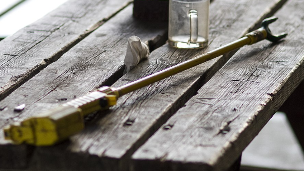 An electric cattle prod lying on a wooden bench with a mug in the background