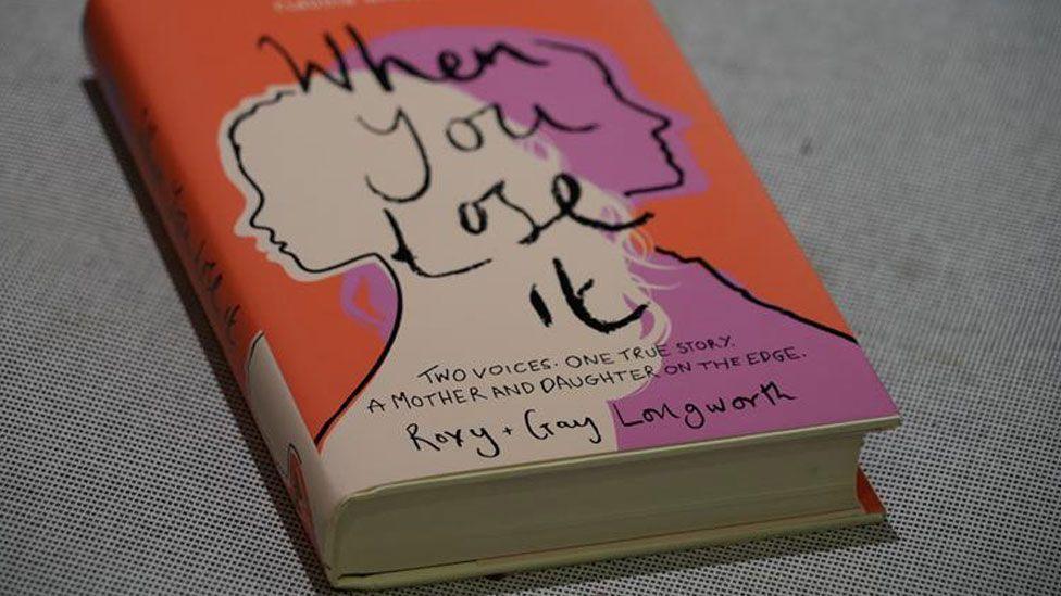 A hardback book resting on a table. it has a pink, cream and orange cover with two line silhouettes of a girl and a mother, back to back. Overlaid on in black lettering are the words when you lose it. 
