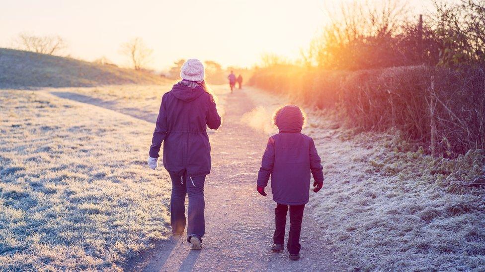 A mother and her young son walking to school through a frosty park in winter.