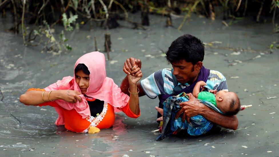 Rohingya refugees carry their child as they walk through water after crossing border by boat through the Naf River in Teknaf, Bangladesh, 7 September 2017