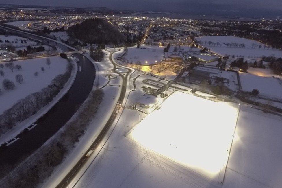 Aerial image of new road and lit up snow-covered rugby pitch