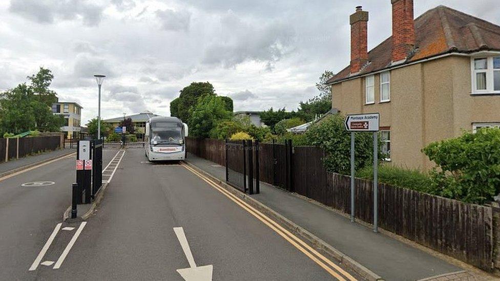 Entrance to school showing direction arrows, gates, and a bus by the side of the road