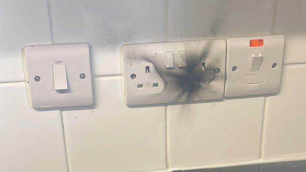 A plug socket that has blown and is covered in soot