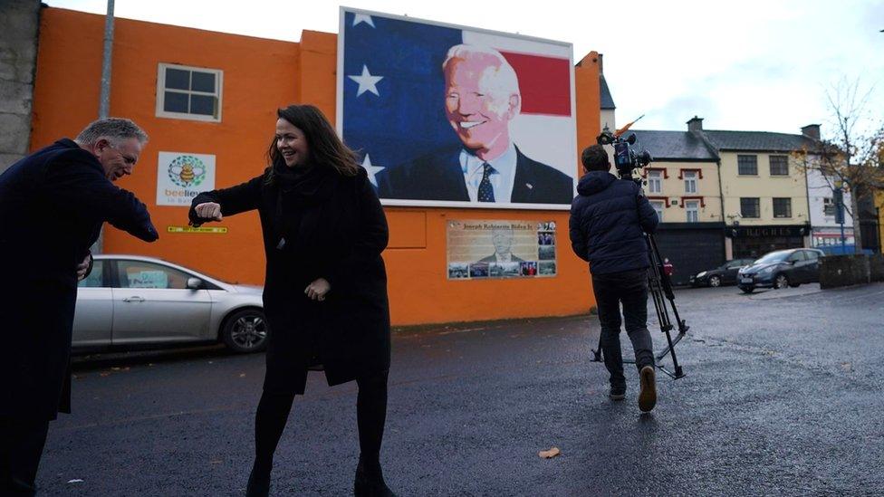 Laurita Blewitt 'elbow bumps' a news crew in Ballina beside a mural of Joe Biden