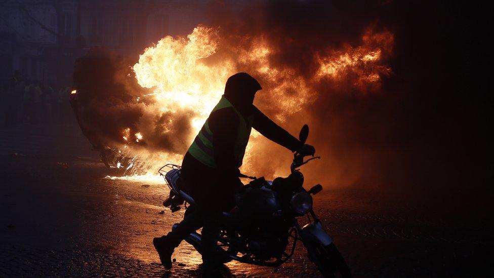 Overturned cars burn, as protesters wearing yellow vests (gilets jaunes) clash with riot police near the Arc de Triomphe as part of a demonstration over high fuel prices on the Champs Elysee in Paris, France