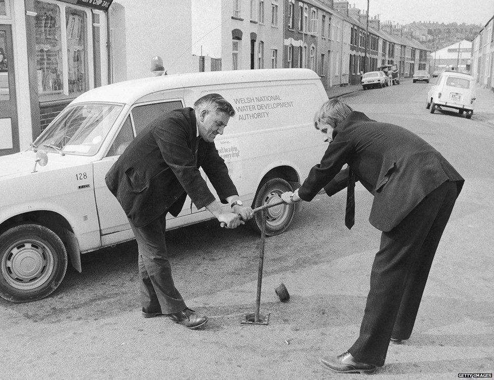 Two men from the Welsh National Water Development Authority turn off the local supply in Gwent at 7pm, to be reconnected at 8am the next day