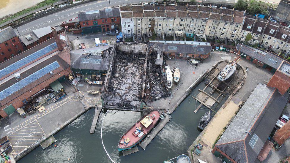 An aerial image taken above the burnt shell of where the Underfall Yard buildings once stood. There is lots of charred debris and wood lying on the ground, the roof is gone and the inside has been gutted by fire. 