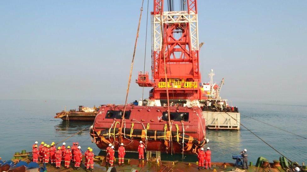 A handout picture provided by the South Korean Ministry of Oceans and Fisheries on 13 June 2016 shows workers from China"s state-run Shanghai Salvage striving to raise the bow of the sunken ferry Sewol by using a huge sea crane in waters off the island of Jindo, southern South Korea, 12 June 2016.