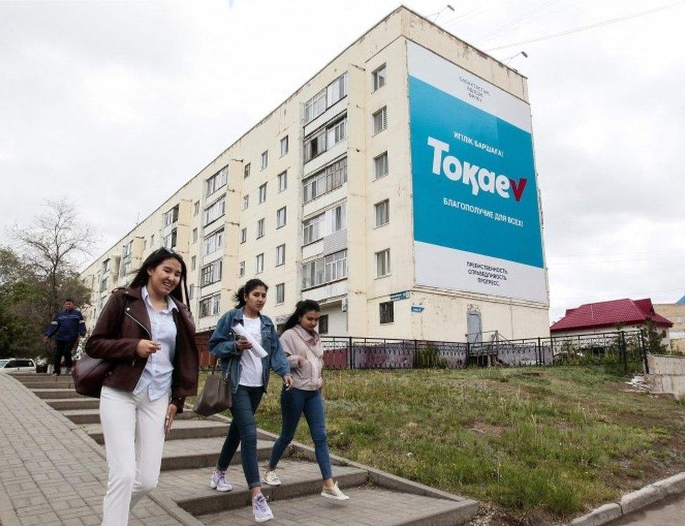 Young women walk past an election campaign billboard for Kazakh President and presidential candidate Kassym-Jomart Tokayev in Nur-Sultan on June 5, 2019, ahead of Kazakhstan"s presidential elections on June 9.