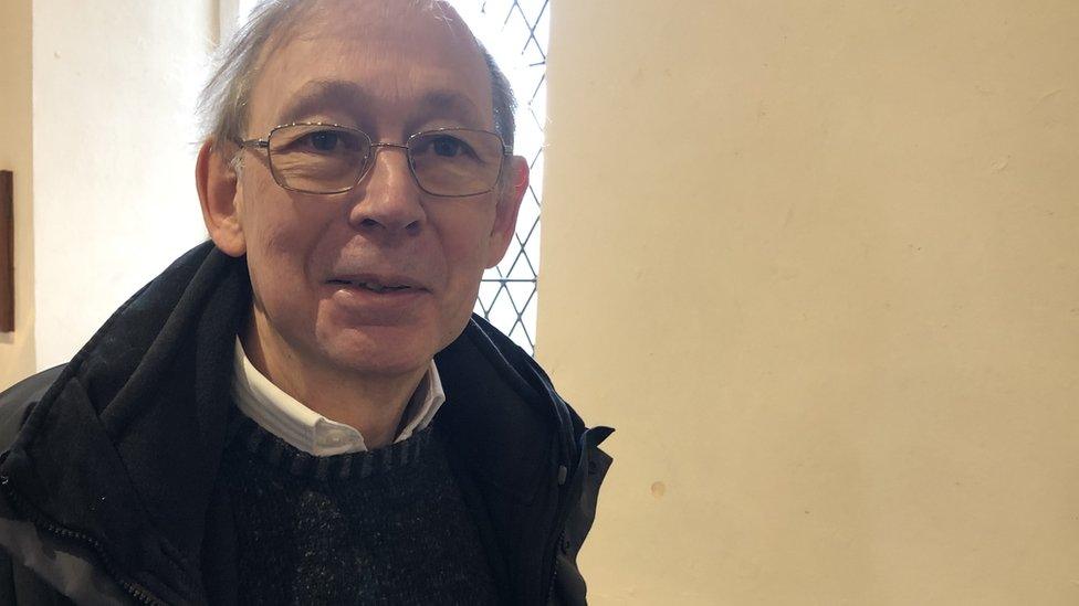 A man with glasses sat in front of a church window