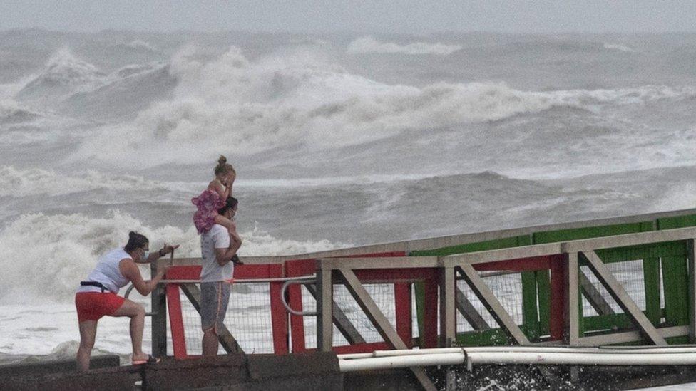 A girl covers her face from strong winds as her family members watch high swells from Hurricane Hanna from a jetty in Galveston, Texas