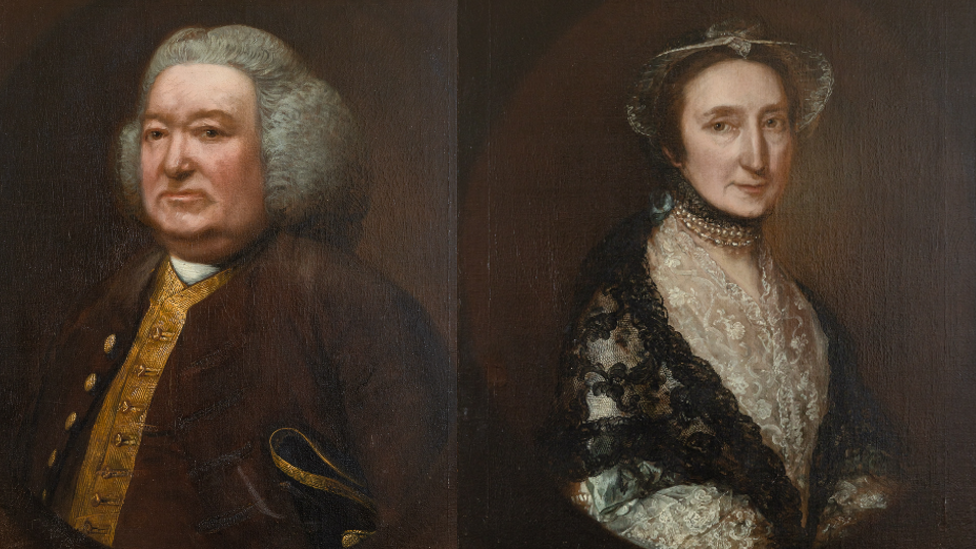 Two paintings of Humphrey Tugwell (1704-1775 and Elizabeth Tugwell (1711-1801). They are both wearing regency era outfits, Humphrey is a large man with a wig, gold waistcoat and brown jacket. Elizabeth has a black shawl and a white dress and bonnet on.
