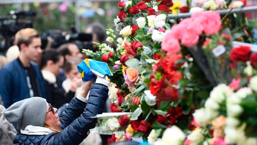 A woman lays a Swedish flag at a makeshift memorial near the site